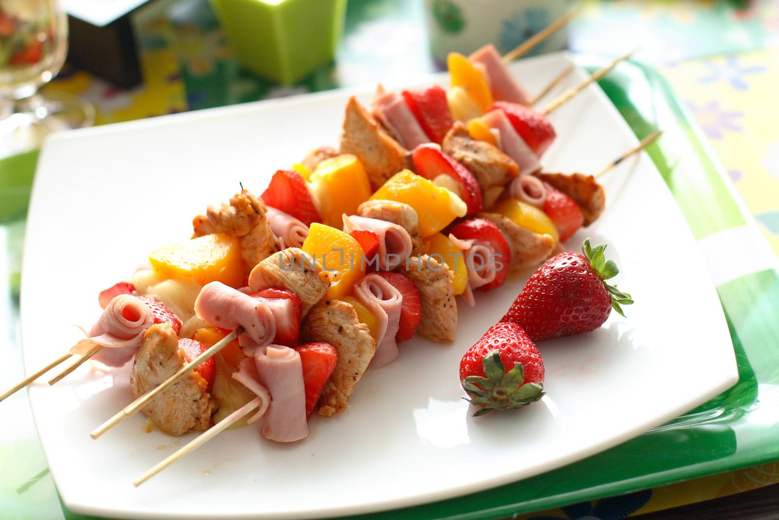 Colorful skewers of chicken, strawberries and pineapple on a white plate