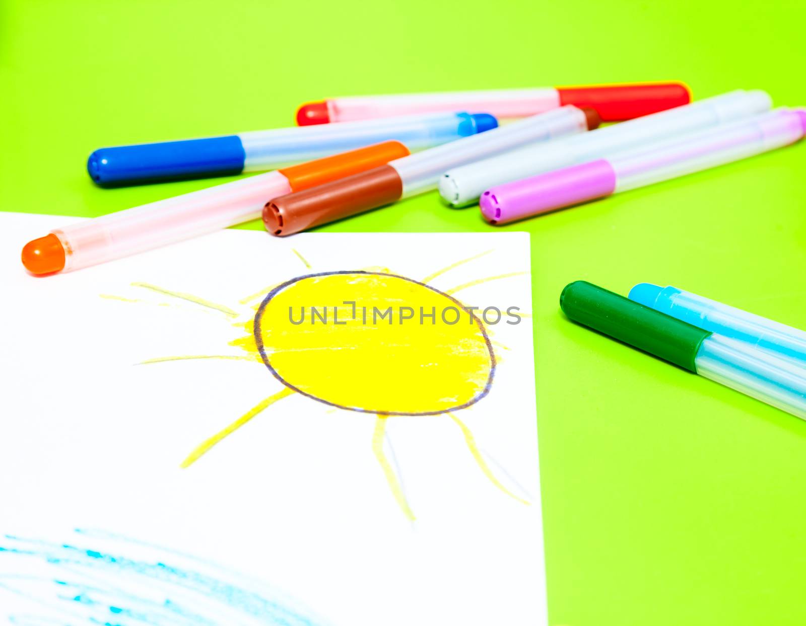 Color markers with child's drawing of the sun on a table