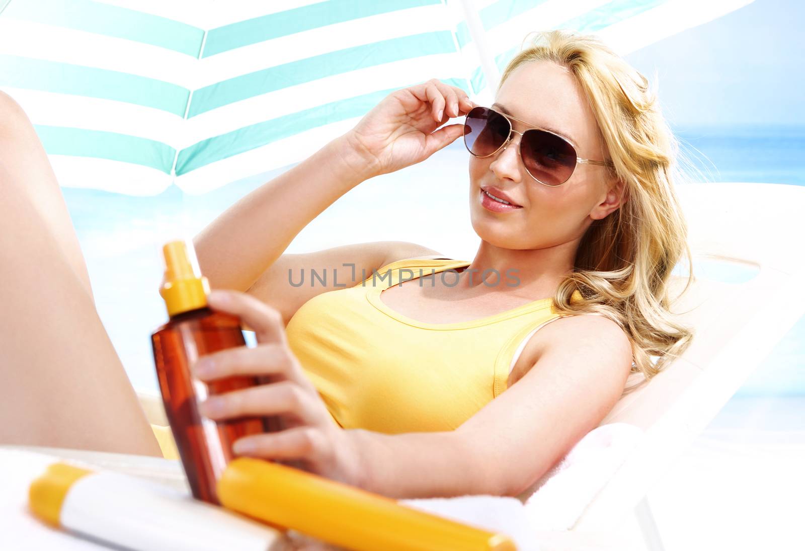 Beautiful blonde woman lying on a lounger hidden from the sun under a blue sunshade.