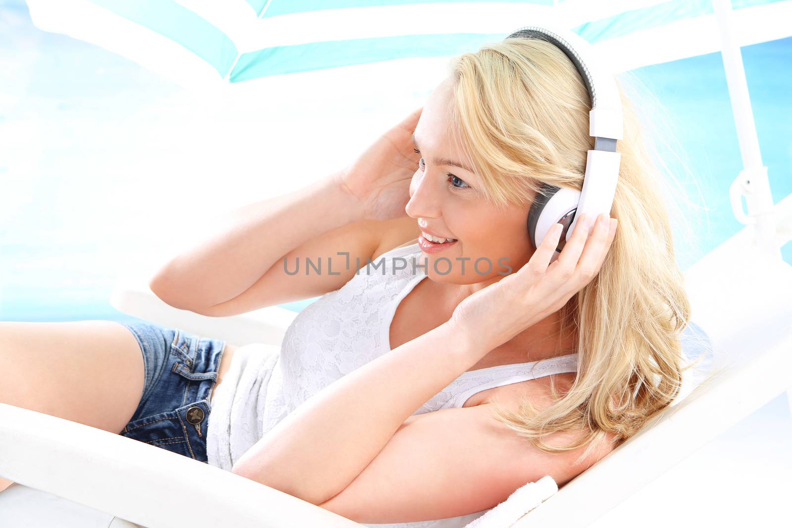 Young attractive woman relaxing on a deck chair relaxing listening to music on a background of blue ocean .