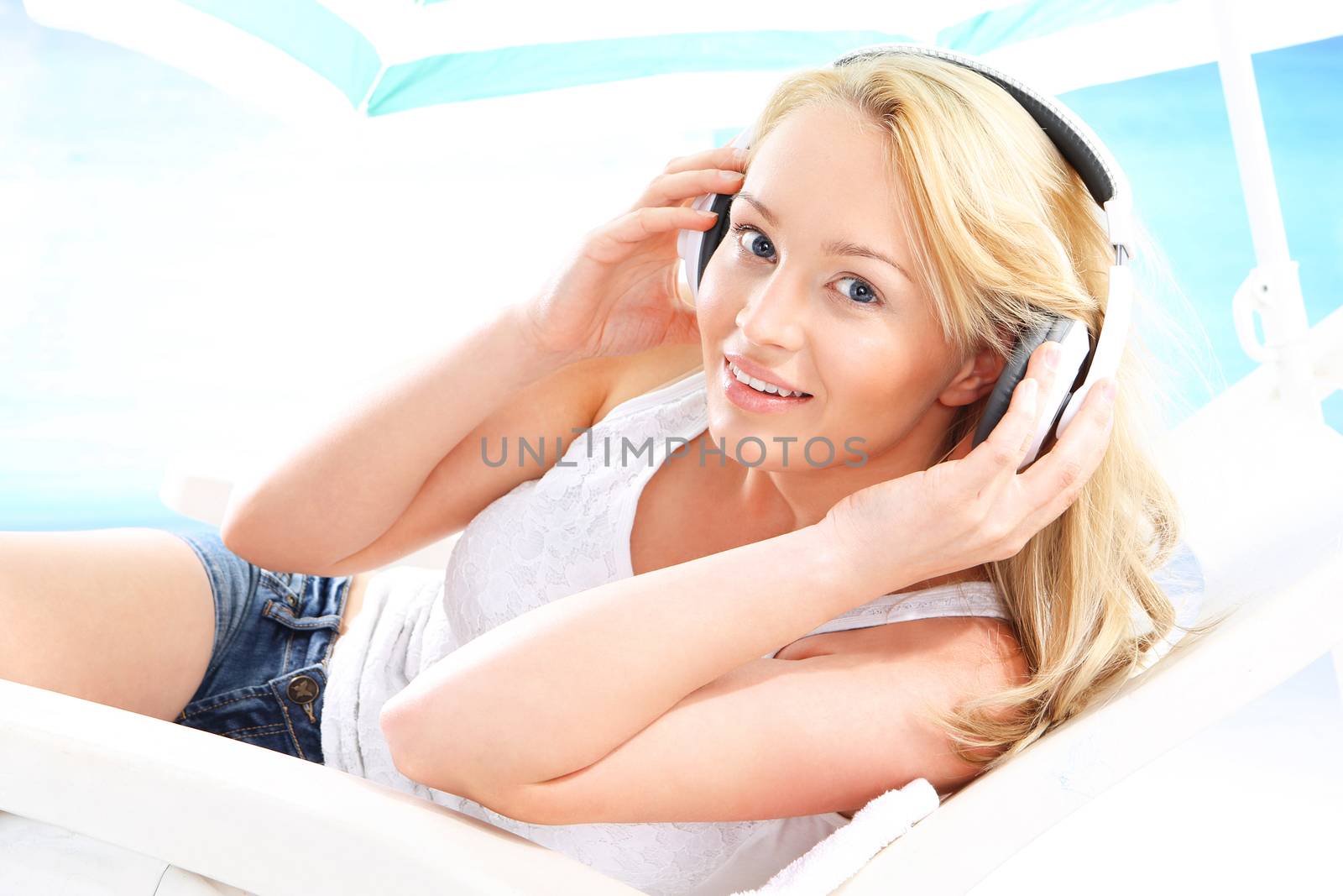 Young attractive woman relaxing on a deck chair relaxing listening to music on a background of blue ocean .