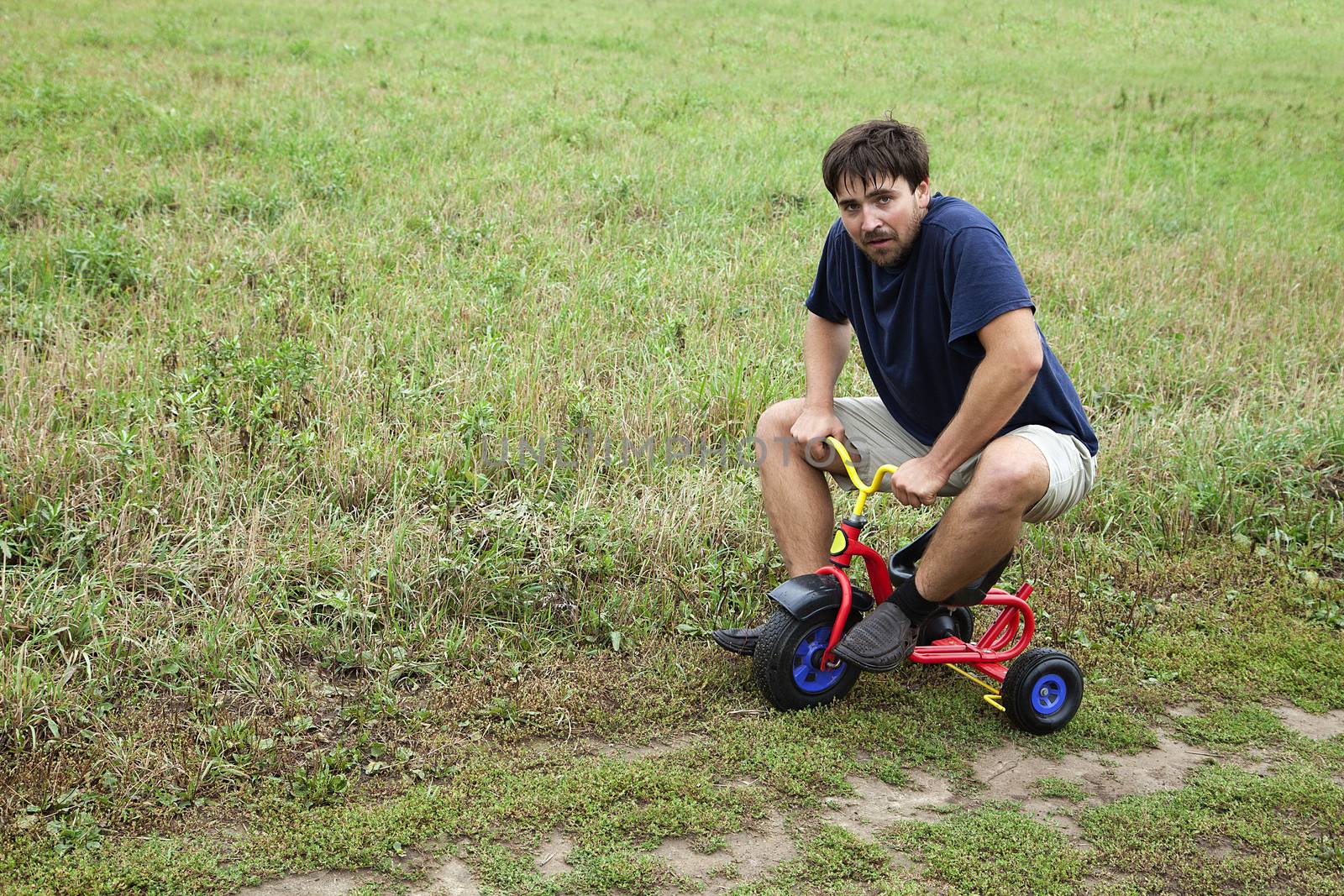 Adult man tying to ride on a small tricycle