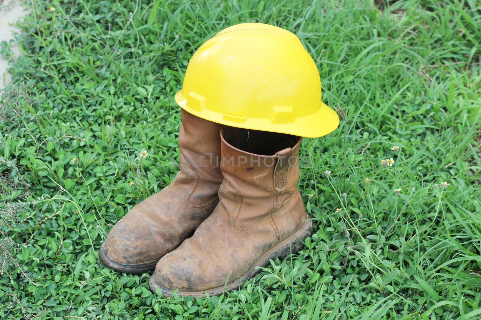 Old brown work boots and hard hat  on green grass by ZONETEEn