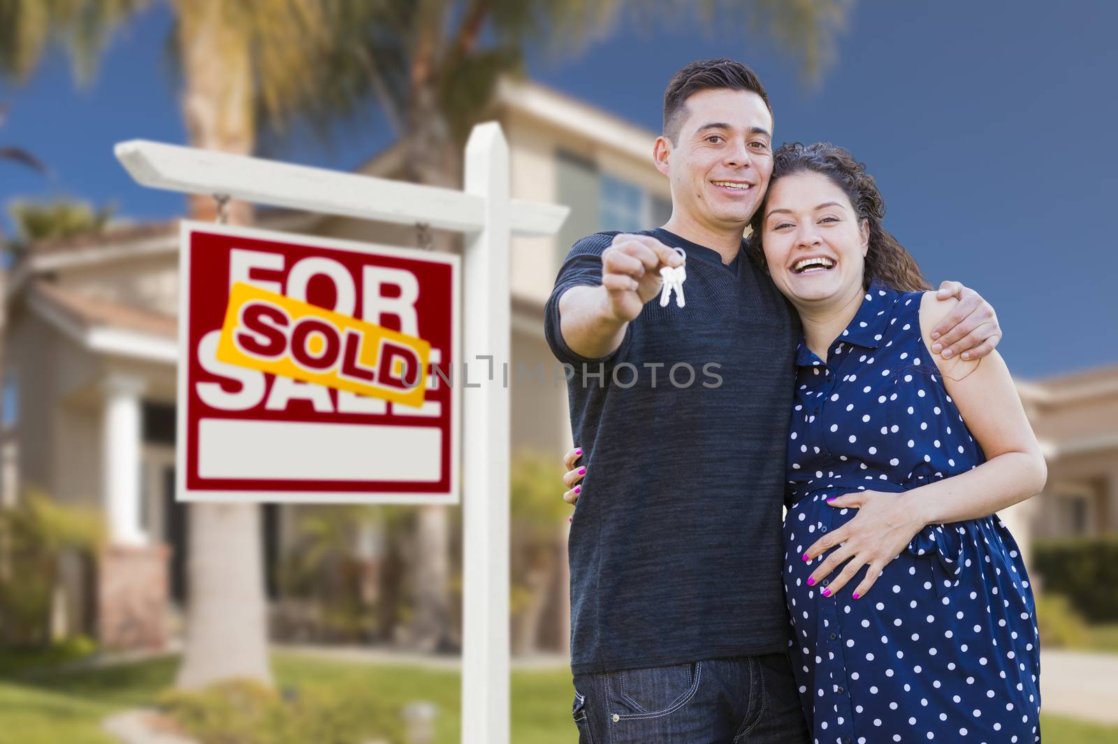 Young Happy Pregnant Hispanic Young Couple with House Keys in Front of Their New Home and Sold For Sale Real Estate Sign.