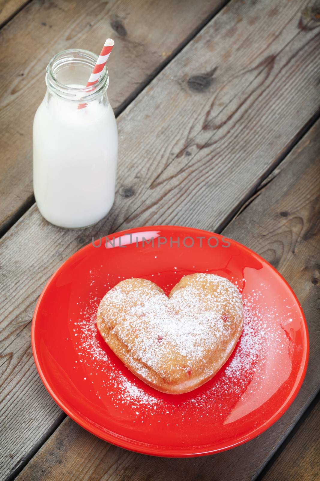 A heart-shaped doughnut sprinkled with icing sugar on a red plate.