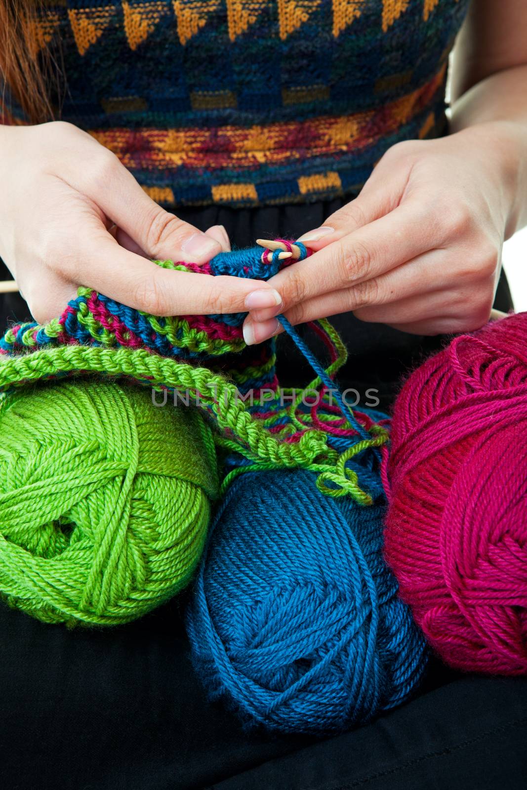 A woman's hands knitting with three colors of yarn.