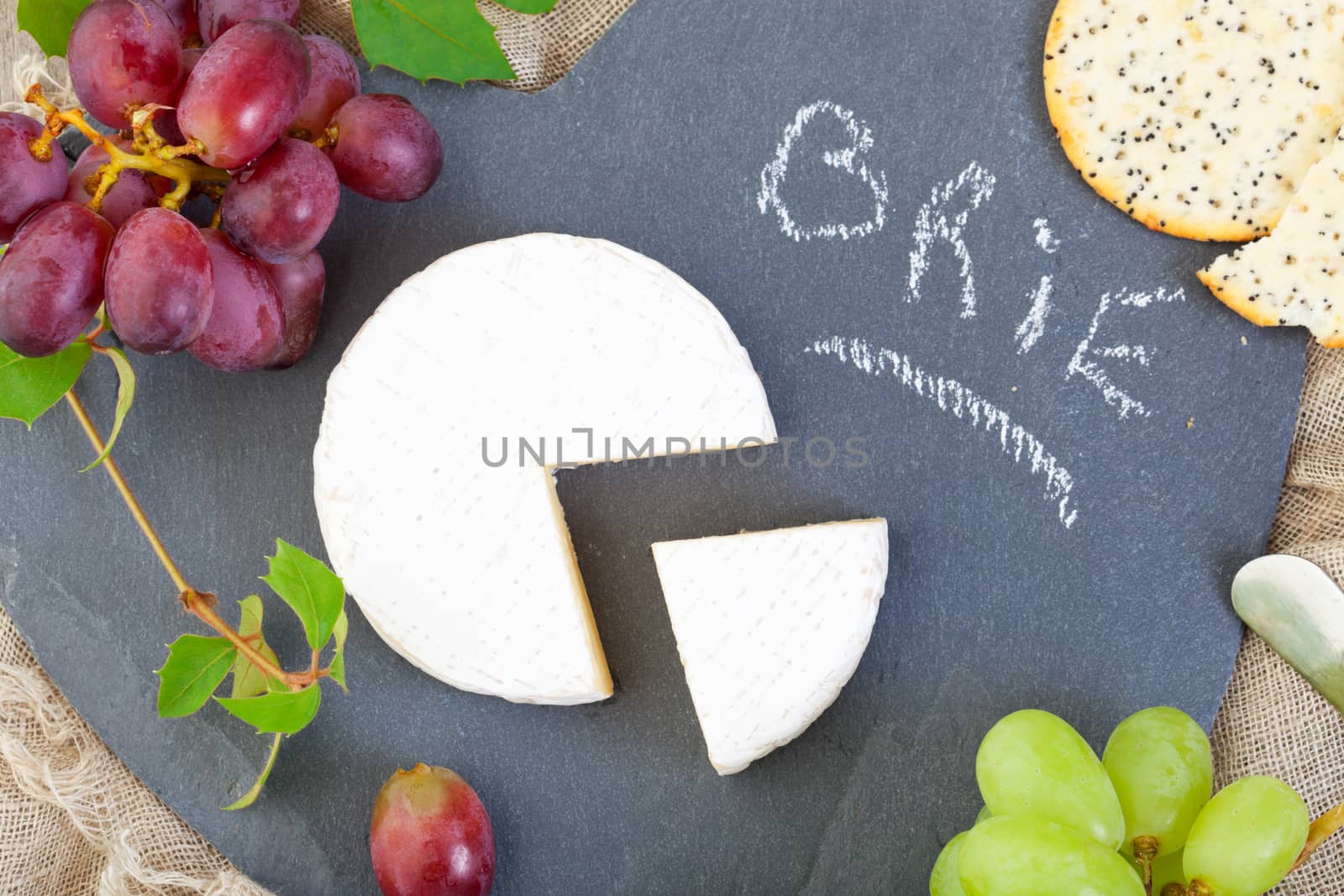 Brie cheese on a heart shaped slate cheese board with grapes and poppy seed crackers.