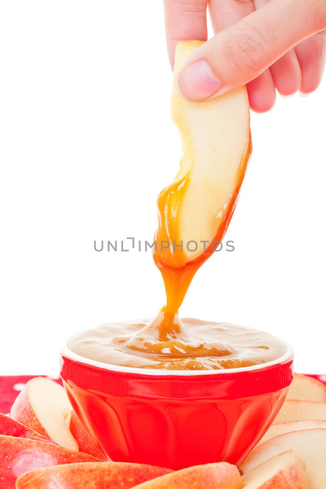 A slice of fresh apple being dipped into smooth, buttery caramel dip.  Shot on white background.