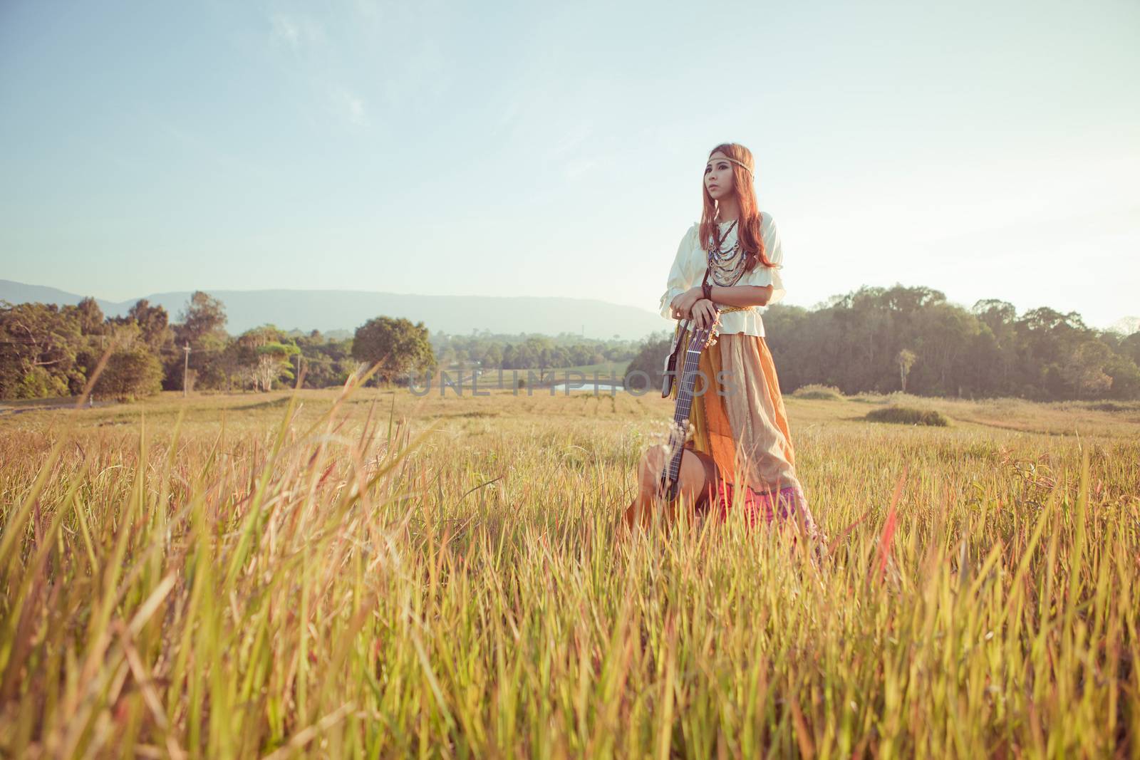 Hippie woman in golden field with acoustic guitar