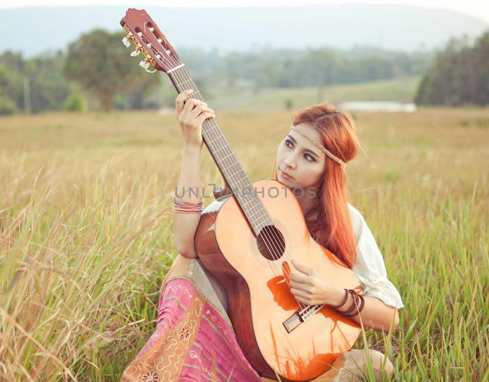 Pretty country hippie girl playing guitar on grass