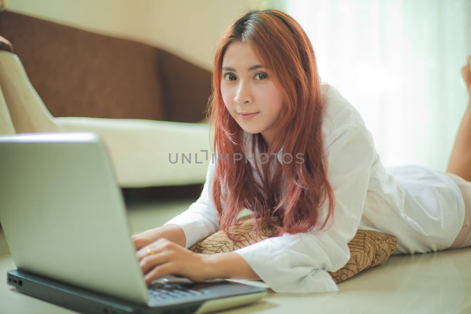 Happy asian young woman lying using laptop at home