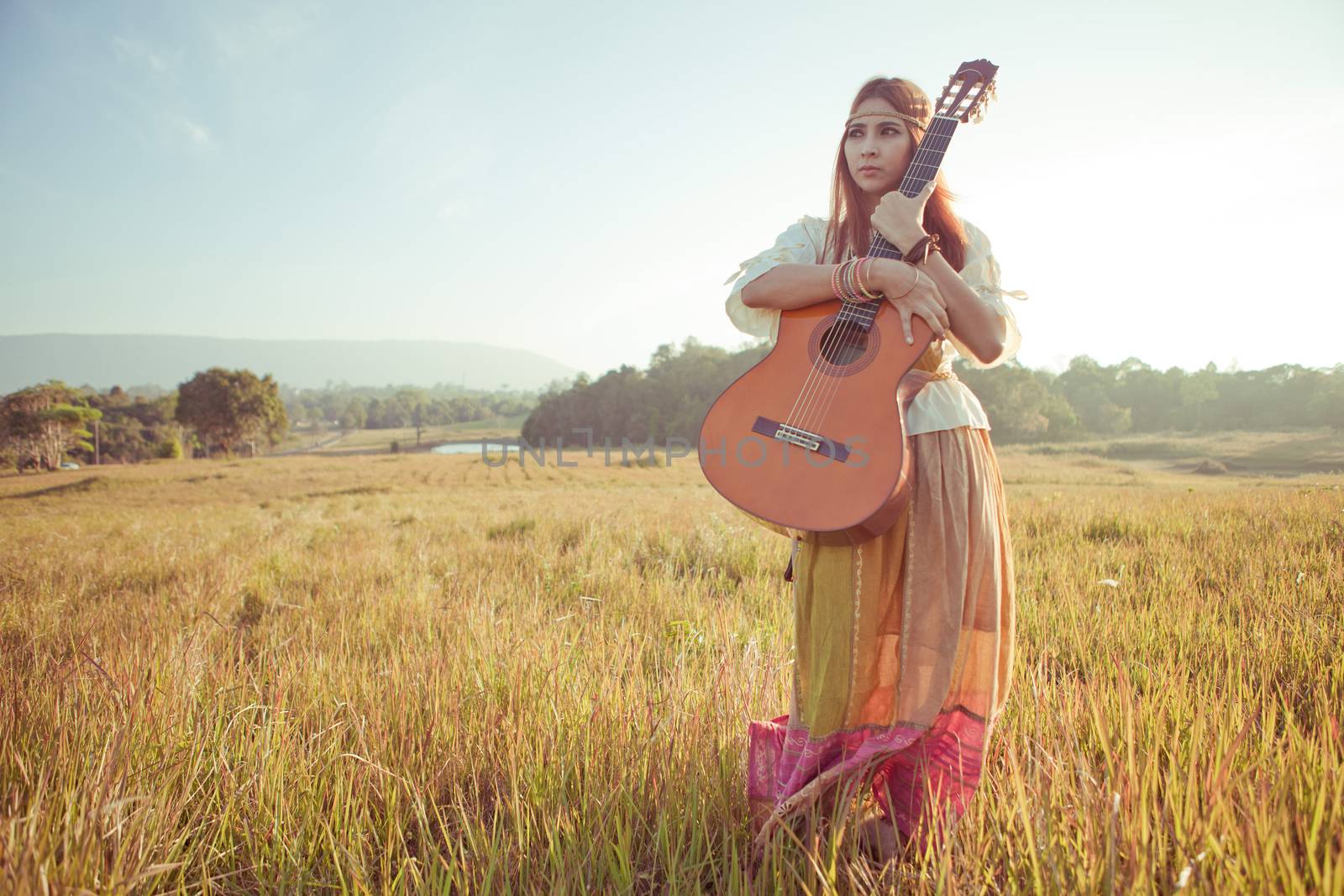 Hippie woman in golden field with acoustic guitar