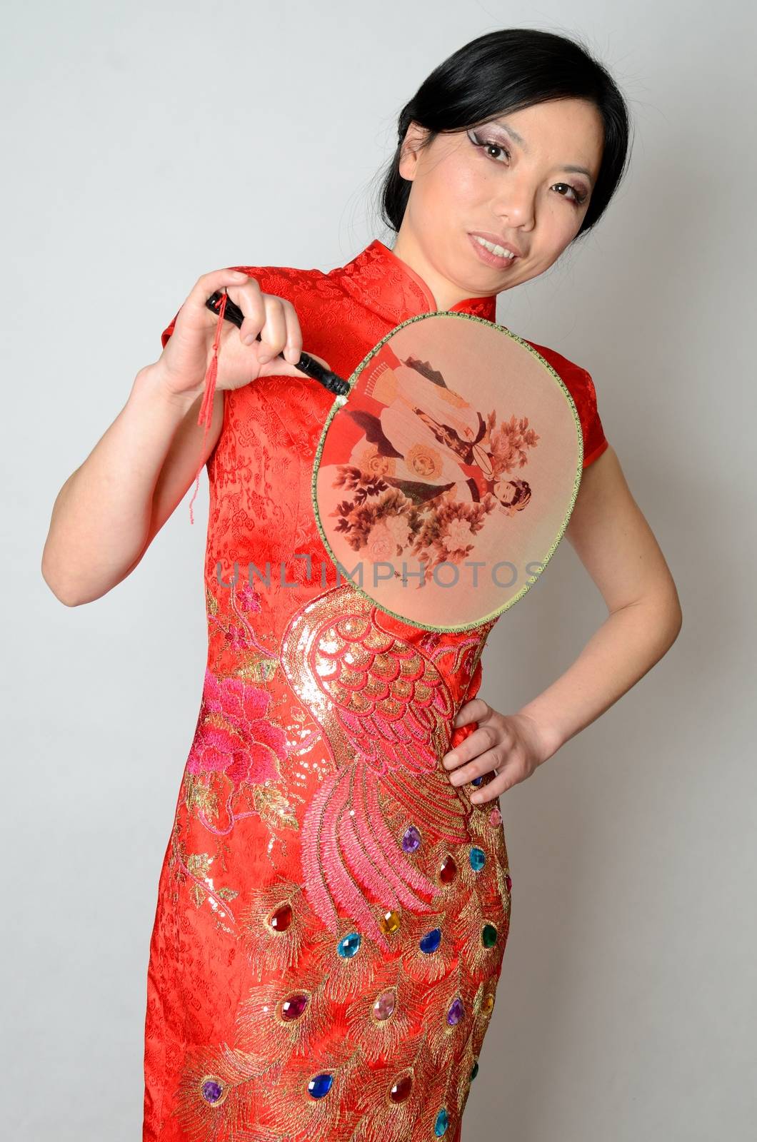 Elegant Chinese lady wearing traditional red dress. Pretty Asian female model holding fan in her hand. 