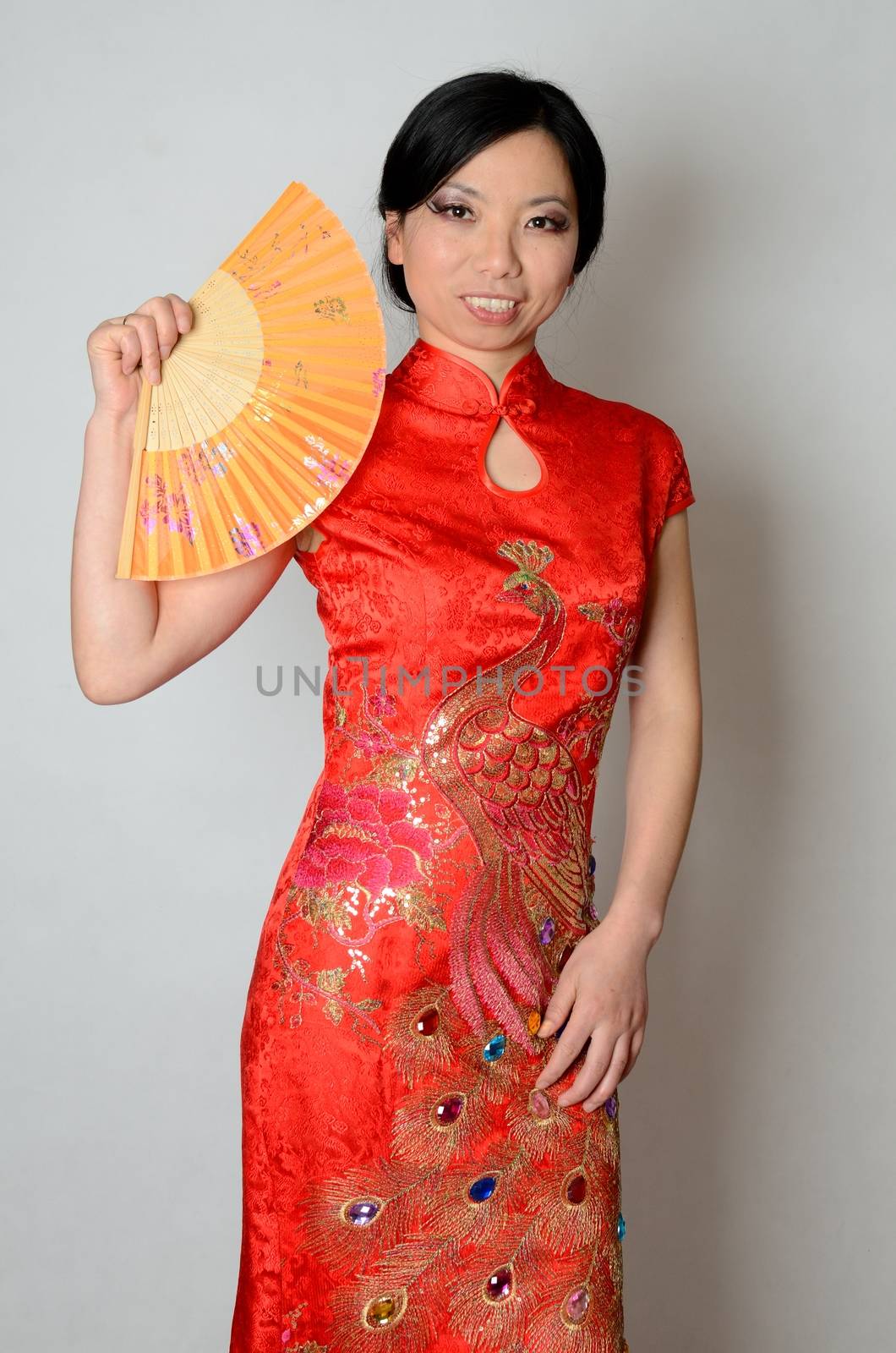 Elegant Chinese lady wearing traditional red dress. Pretty Asian female model holding fan in her hand. 