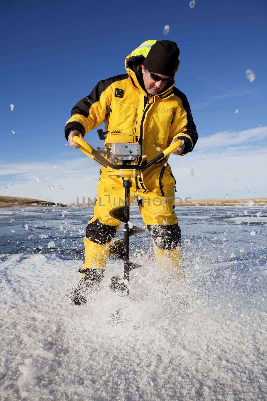 Ice flies everywhere as an ice fisherman uses an auger to make his fishing hole.