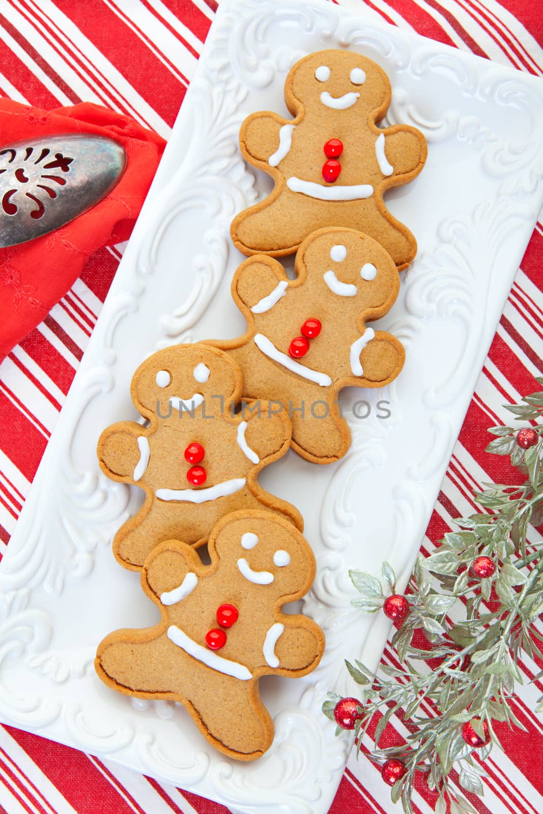 Gingerbread men served on an embossed tray on a candy cane striped tablecloth.