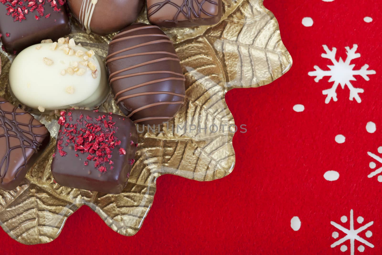 A variety of decandent chocolates arranged on a gold poinsettia plate, on a red felt snowflake mat.