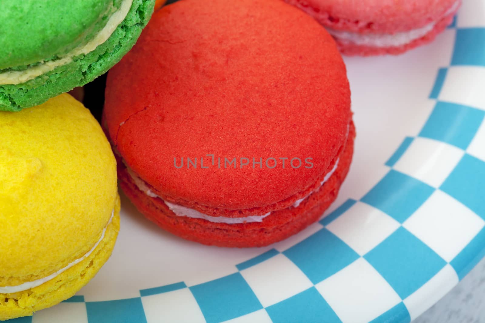 Closeup of brightly colored macaroon cookies on a plate edged in a blue and white checker.