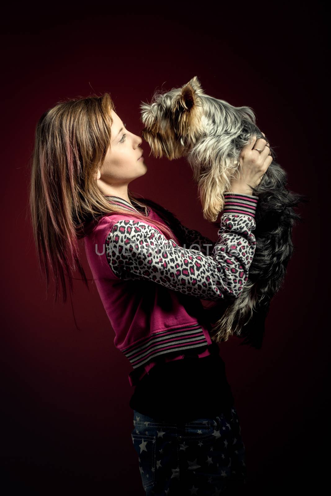 attractive smiling young girl with long hair wearing pink dress with her best friend yorkshire terrier on red background