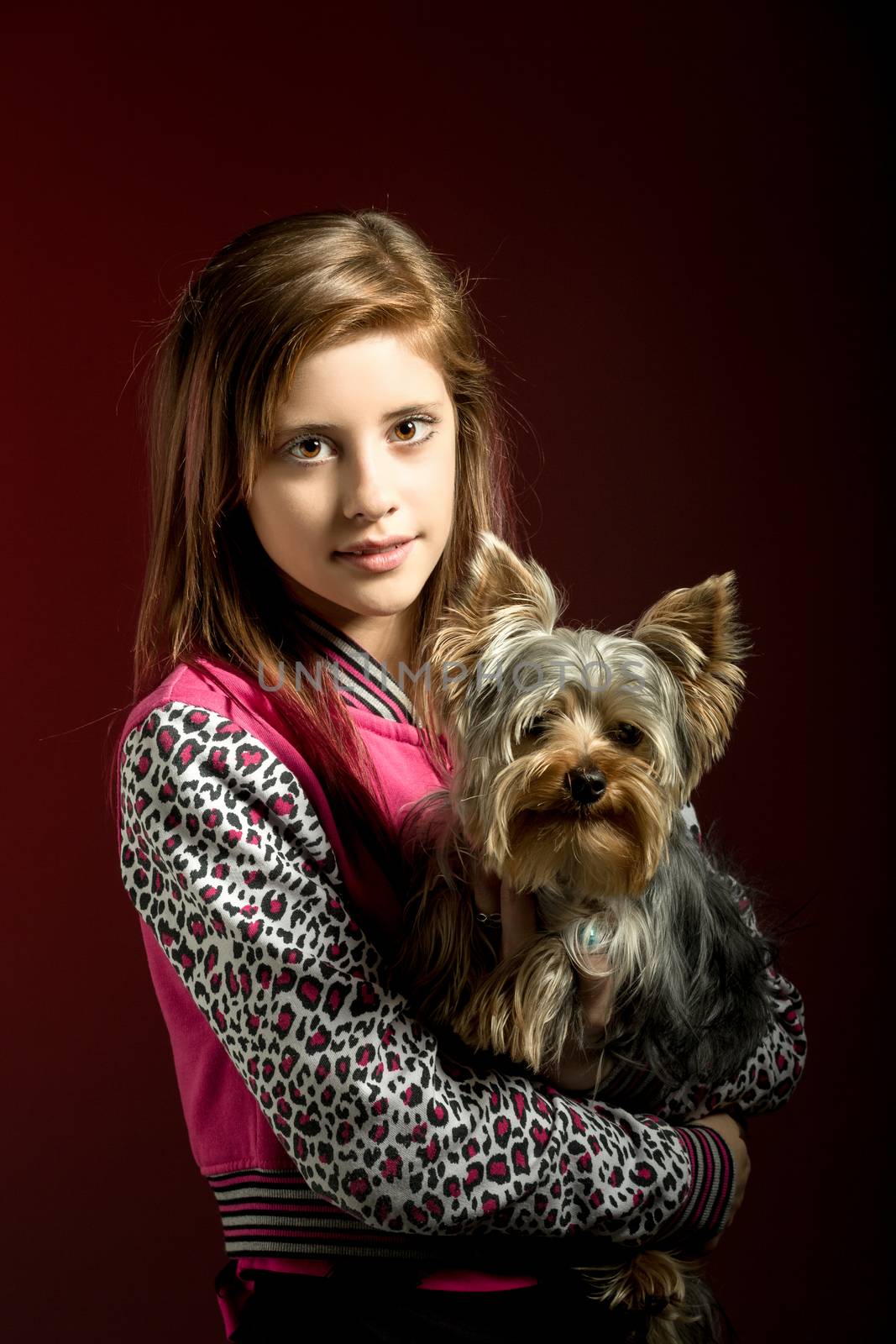 attractive smiling young girl with long hair wearing pink dress with her best friend yorkshire terrier on red background