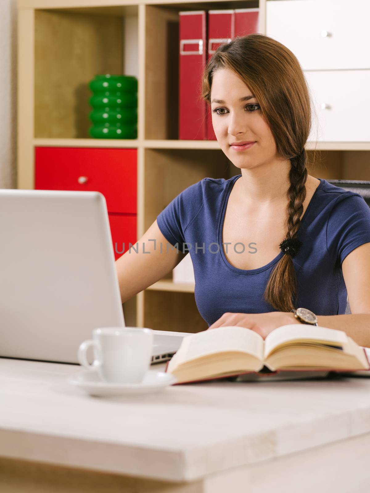 Photo of a beautiful woman using a laptop, drinking coffee, and reading a book.
