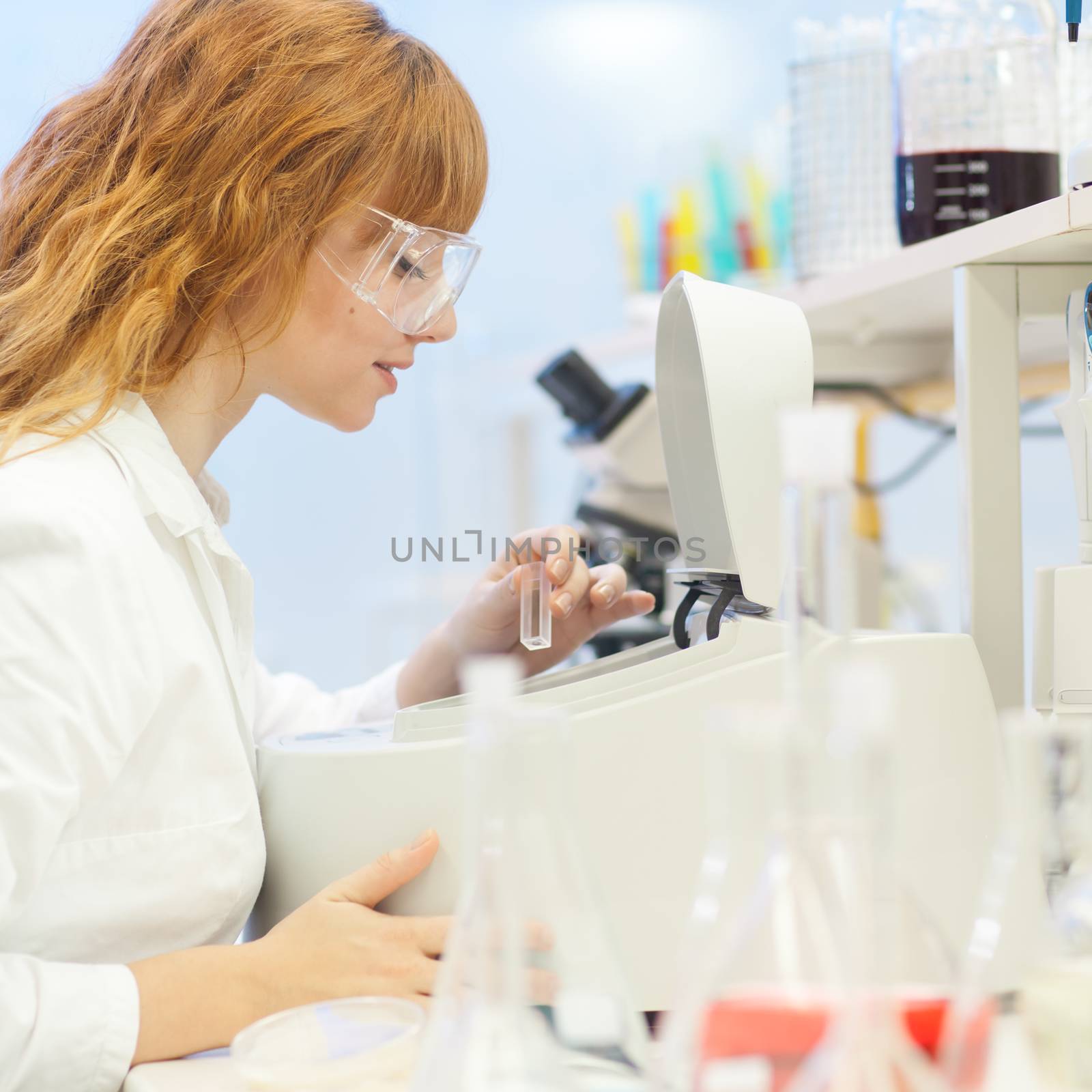 Attractive young PhD student scientist looking at the microscope slide in the life science research laboratory (biochemistry, genetics, forensics, microbiology ..)