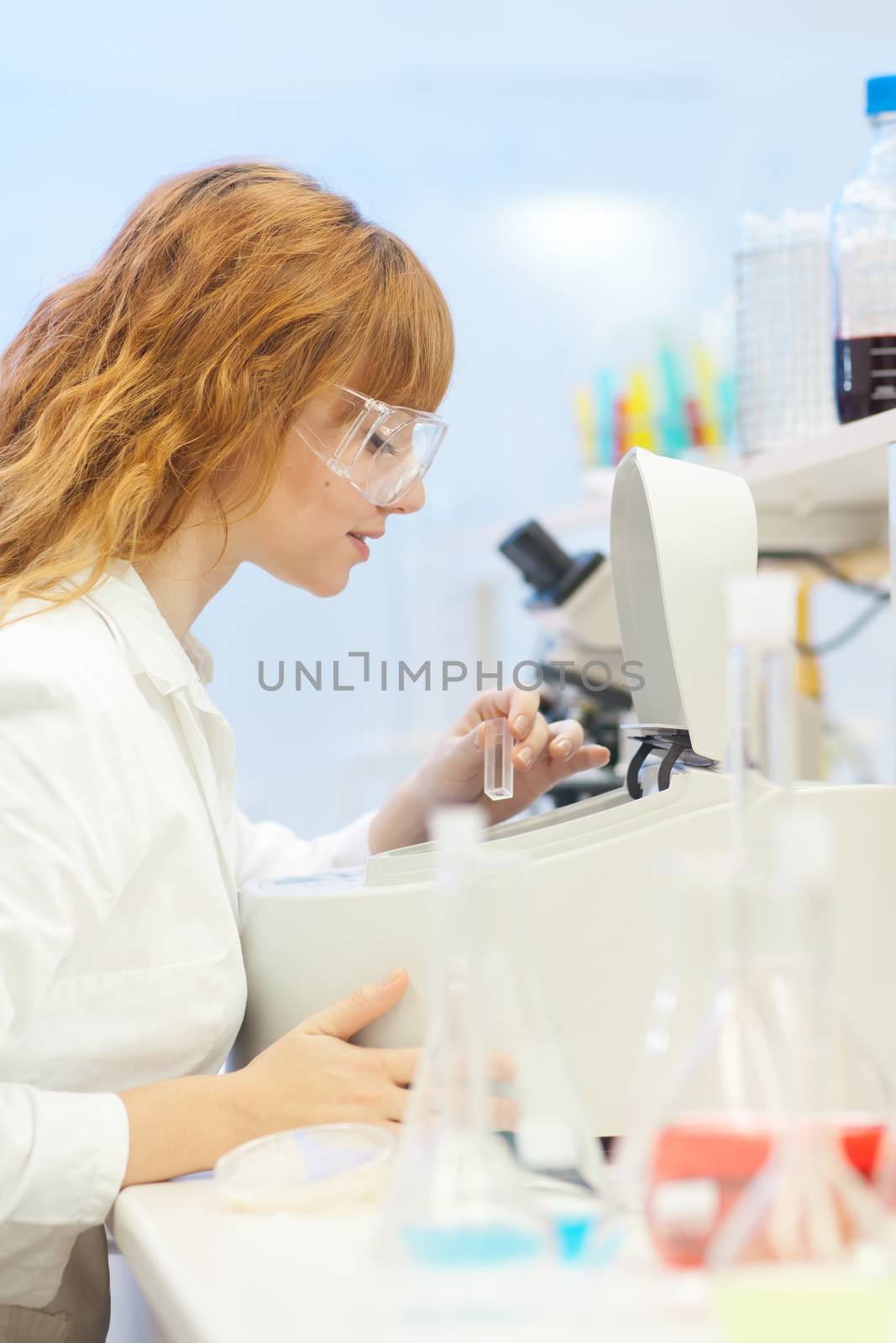 Attractive young PhD student scientist looking at the microscope slide in the life science research laboratory (biochemistry, genetics, forensics, microbiology ..)