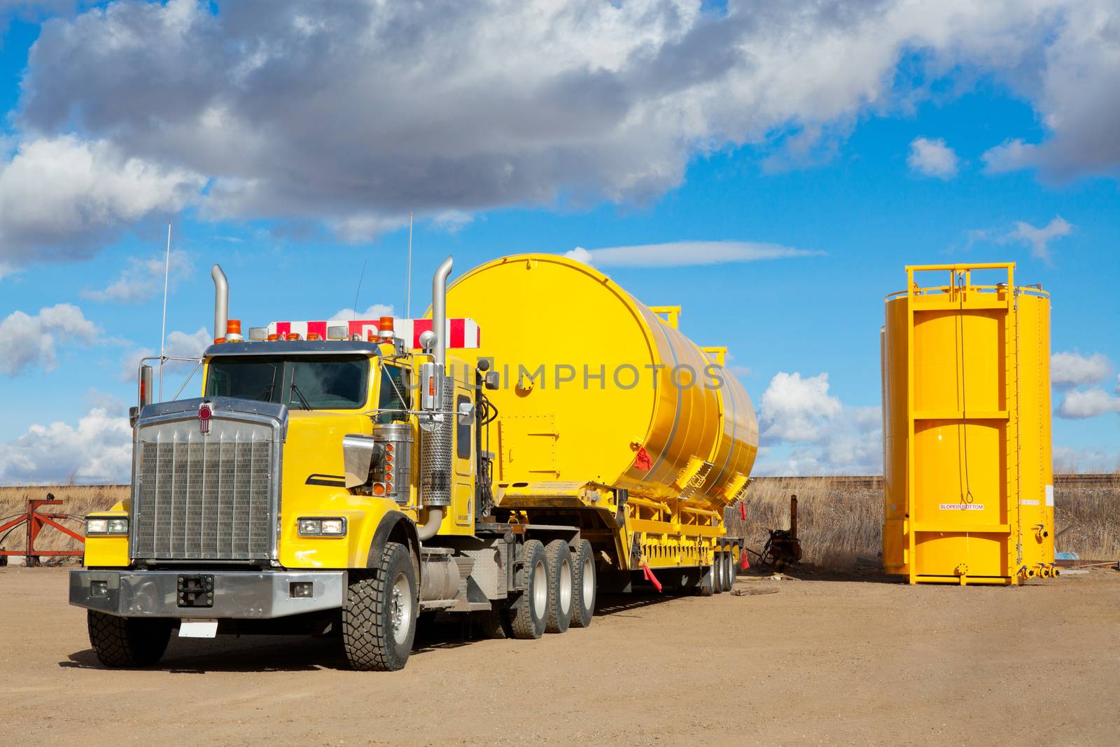 A yellow transport trailer picking up two newly manufactured and coated 400 BBL. oilfield storage tanks.