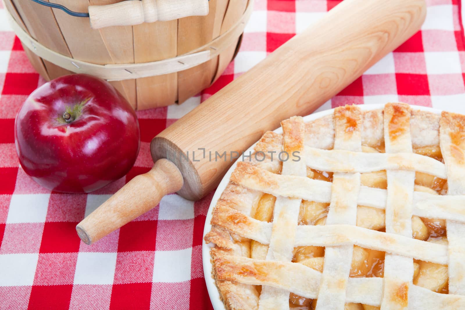 Delicious homemade apple pie cooling next to a rolling pin and a basket of apples.