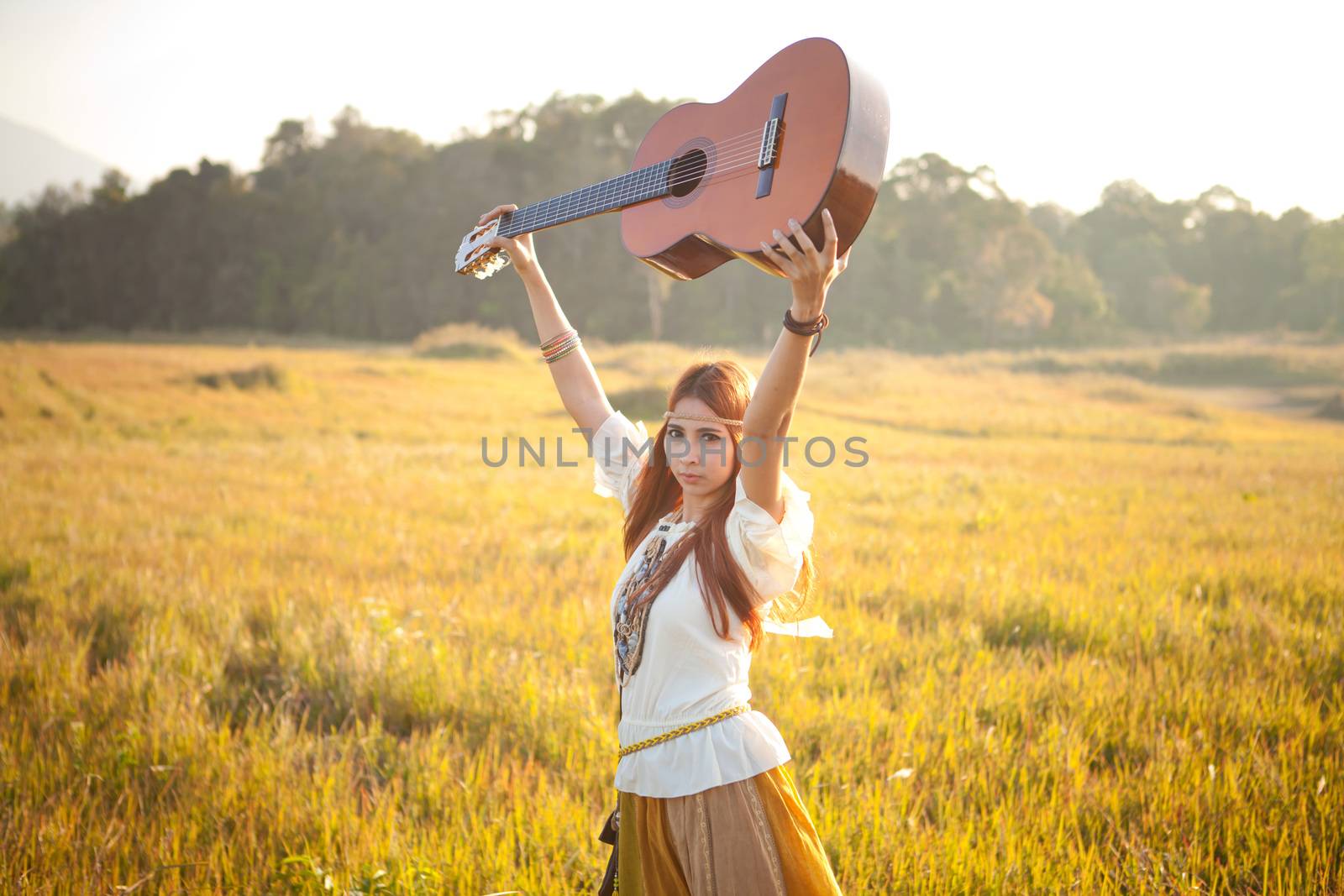 Hippie woman in golden field with acoustic guitar