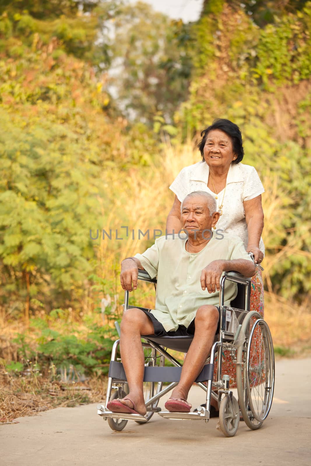 Asian senior woman pushing her disabled hasband on wheelchair