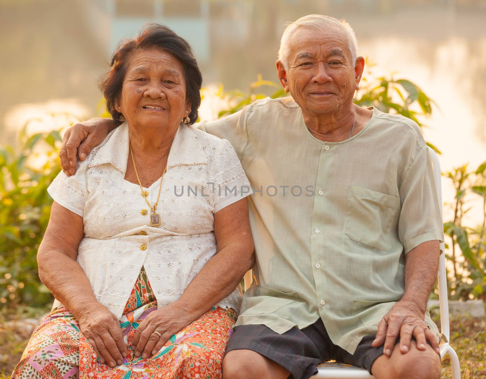 Happy Asian Senior couple sitting outdoors on sunset