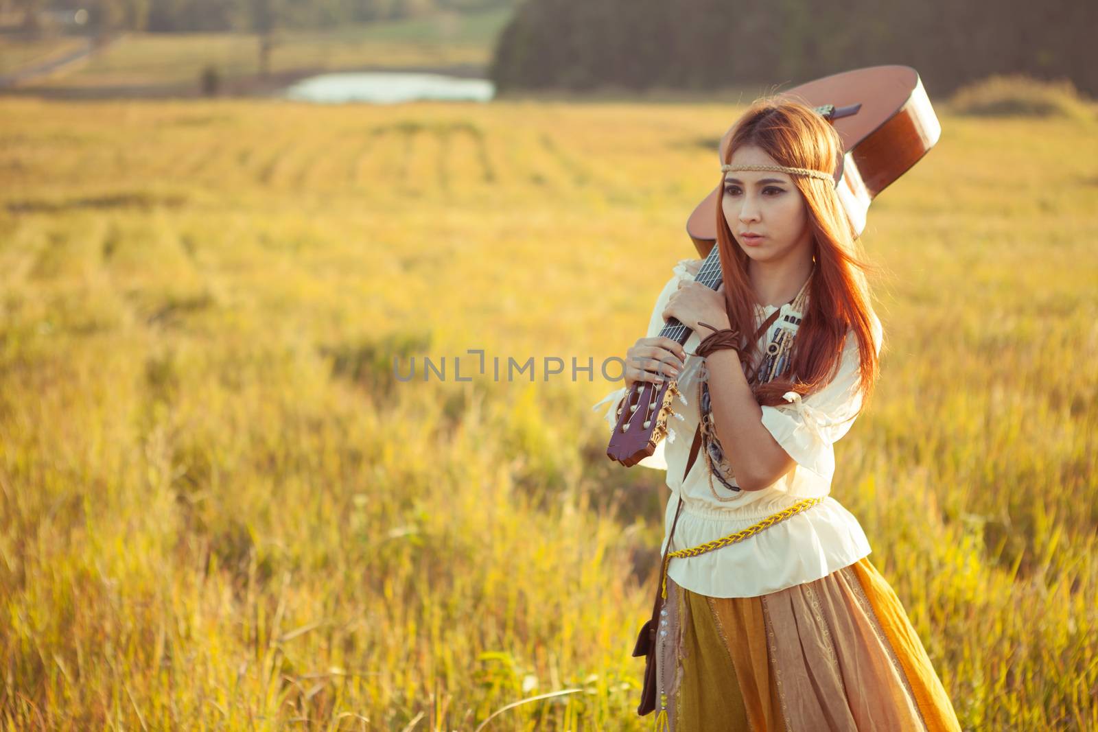 Hippie woman walking in golden field with acoustic guitar