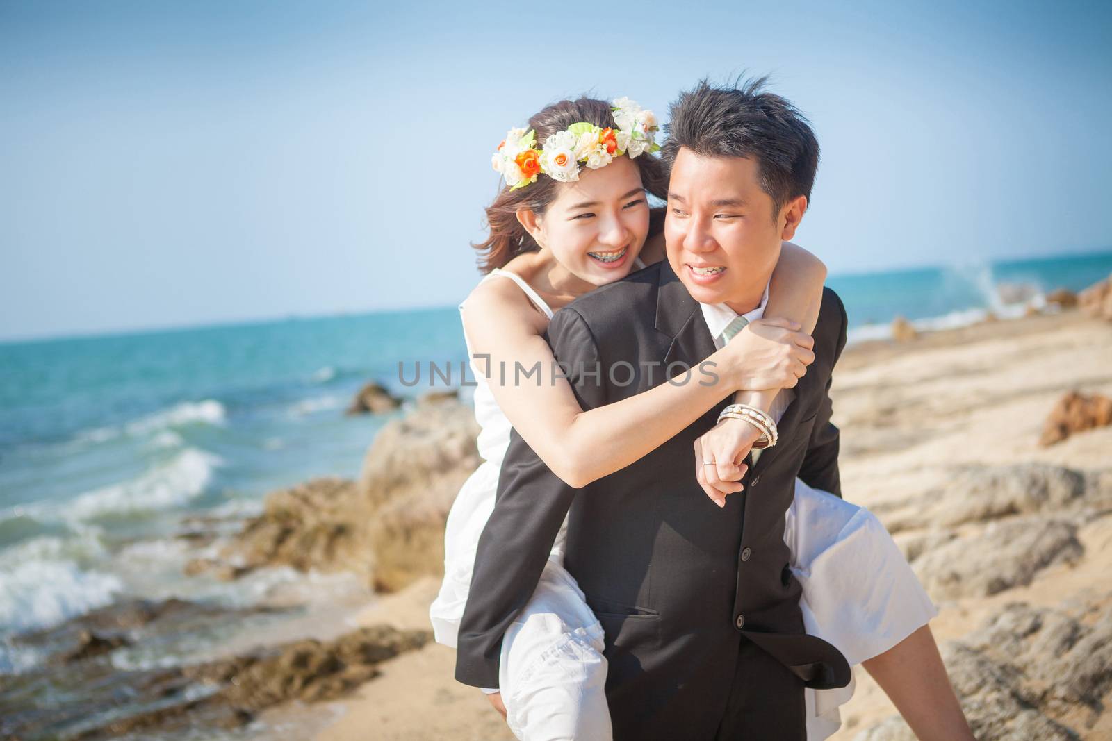 Asian man having his woman piggyback on his back under a blue sky on a beach