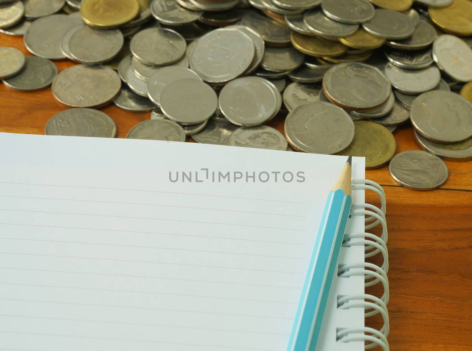 Blue pencil placed on the book, beside that have coins of different sizes stacked together.                            