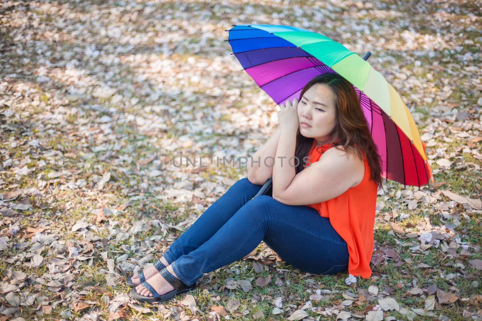 Young asian fat woman sitting with umbrella in autumn park