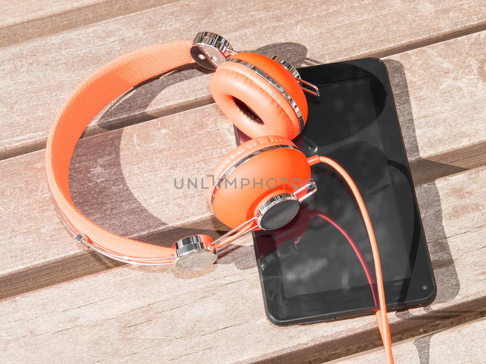 Vibrant orange headphones and black tablet pc on wooden bench for mobile language learning or distance education