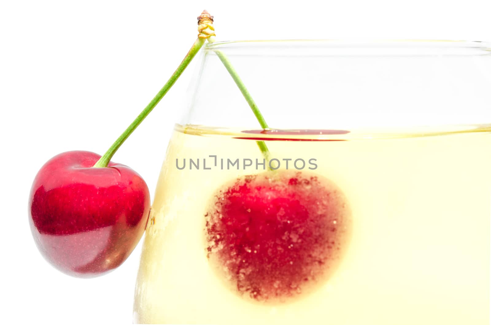Pair ripe cherry berries on top edge of full misted wineglass with cold white wine isolated close-up