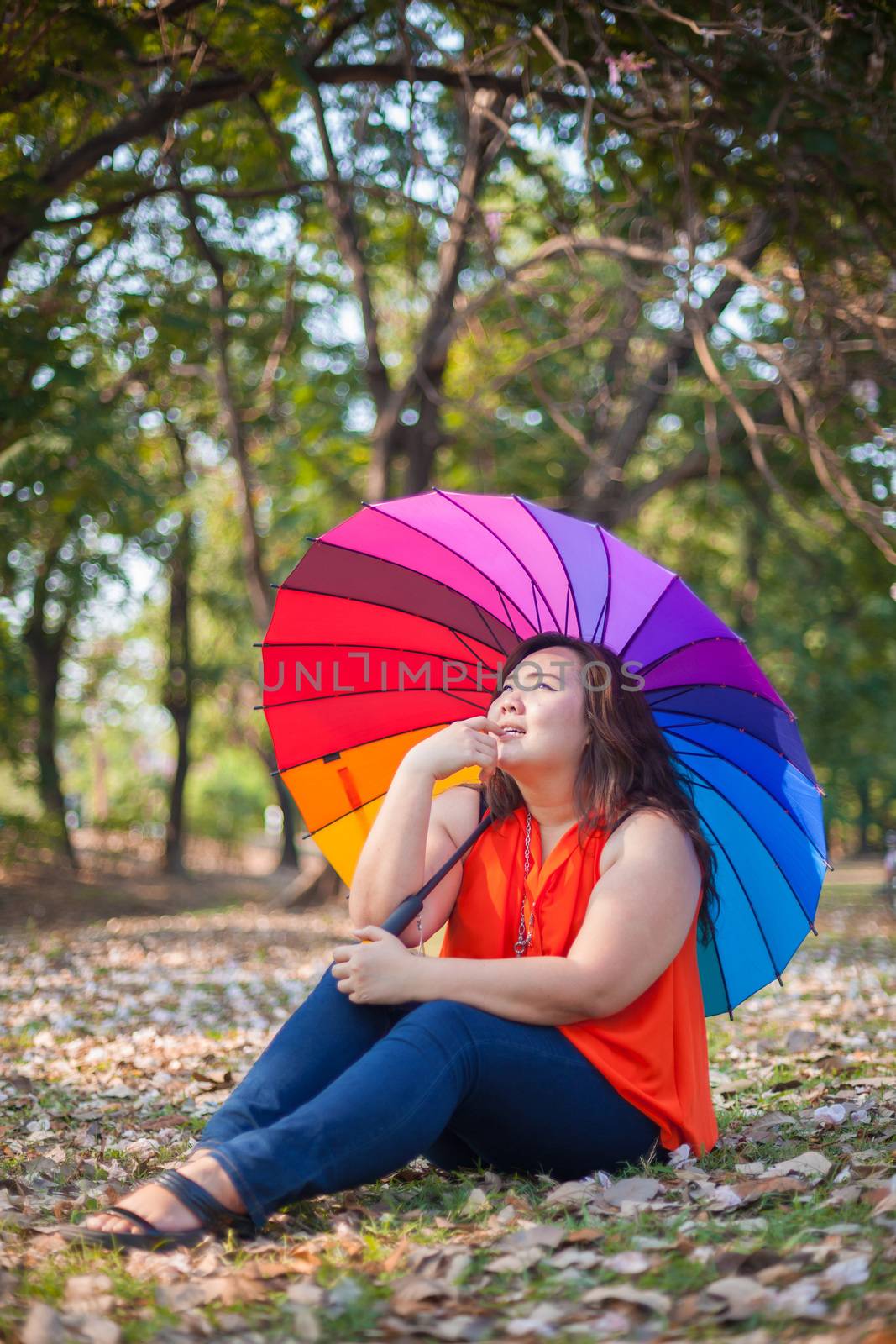 Young asian fat woman sitting with umbrella in autumn park