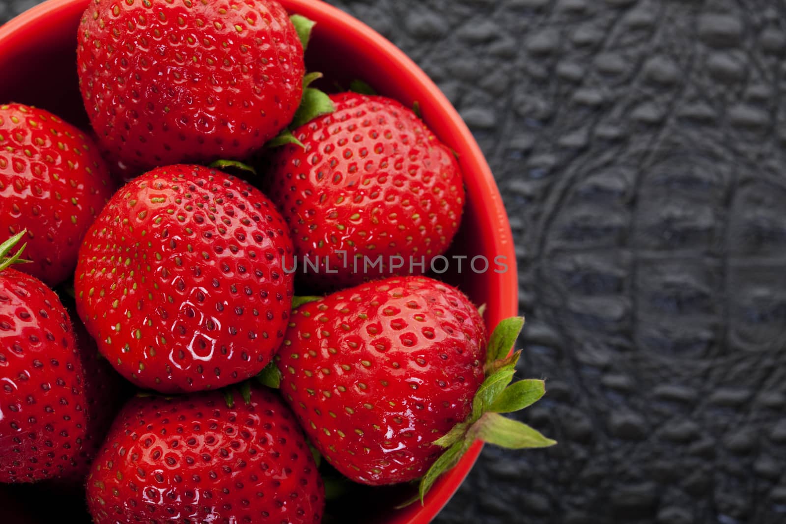 Beautiful, juicy, red strawberries in a red bowl on a black textured background.