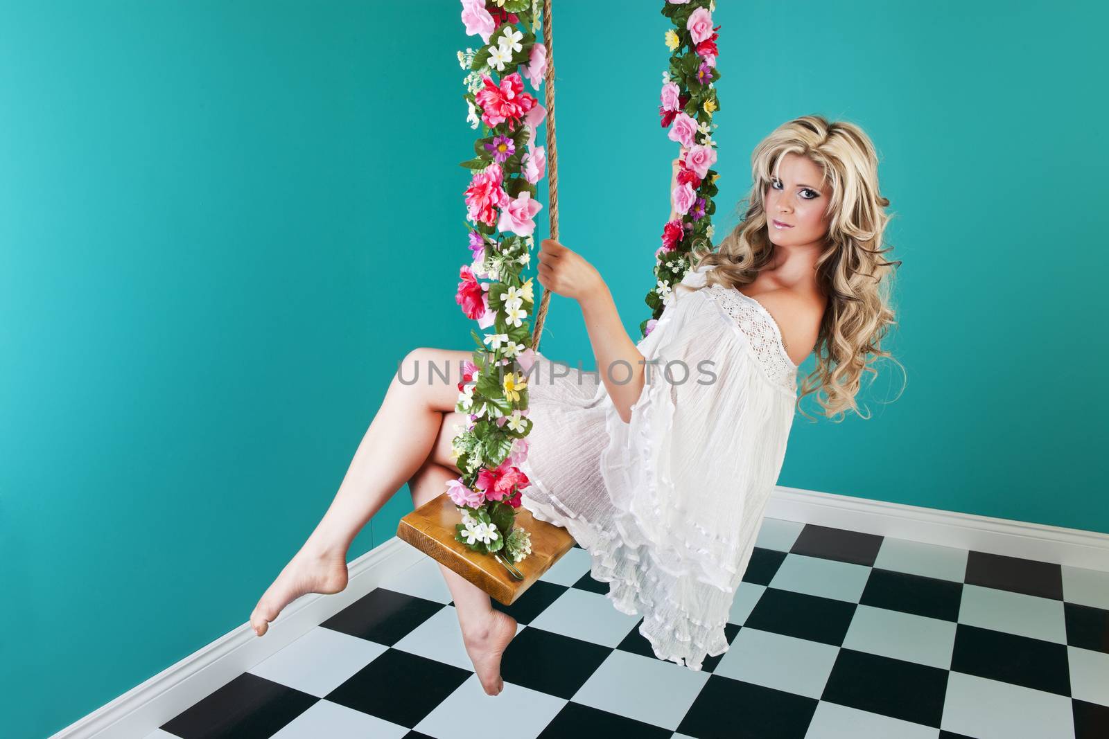 Surreal, fantasy pinup image of a beautiful woman, on a flower covered swing in an empty room.