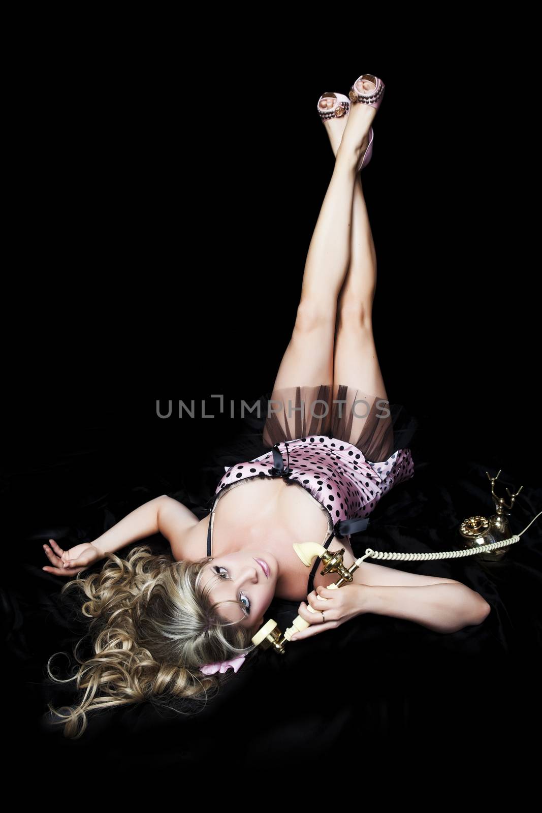 Pretty blond pinup girl in classic pose with telephone.  Black background.