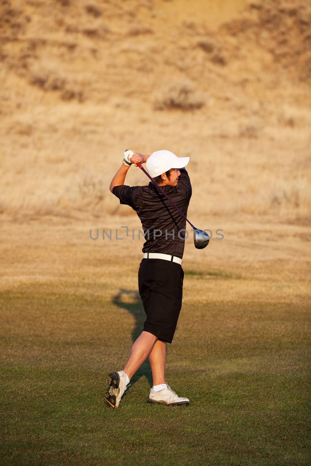 A skilled, mixed-race teenager playing golf.  Shot in early evening light.