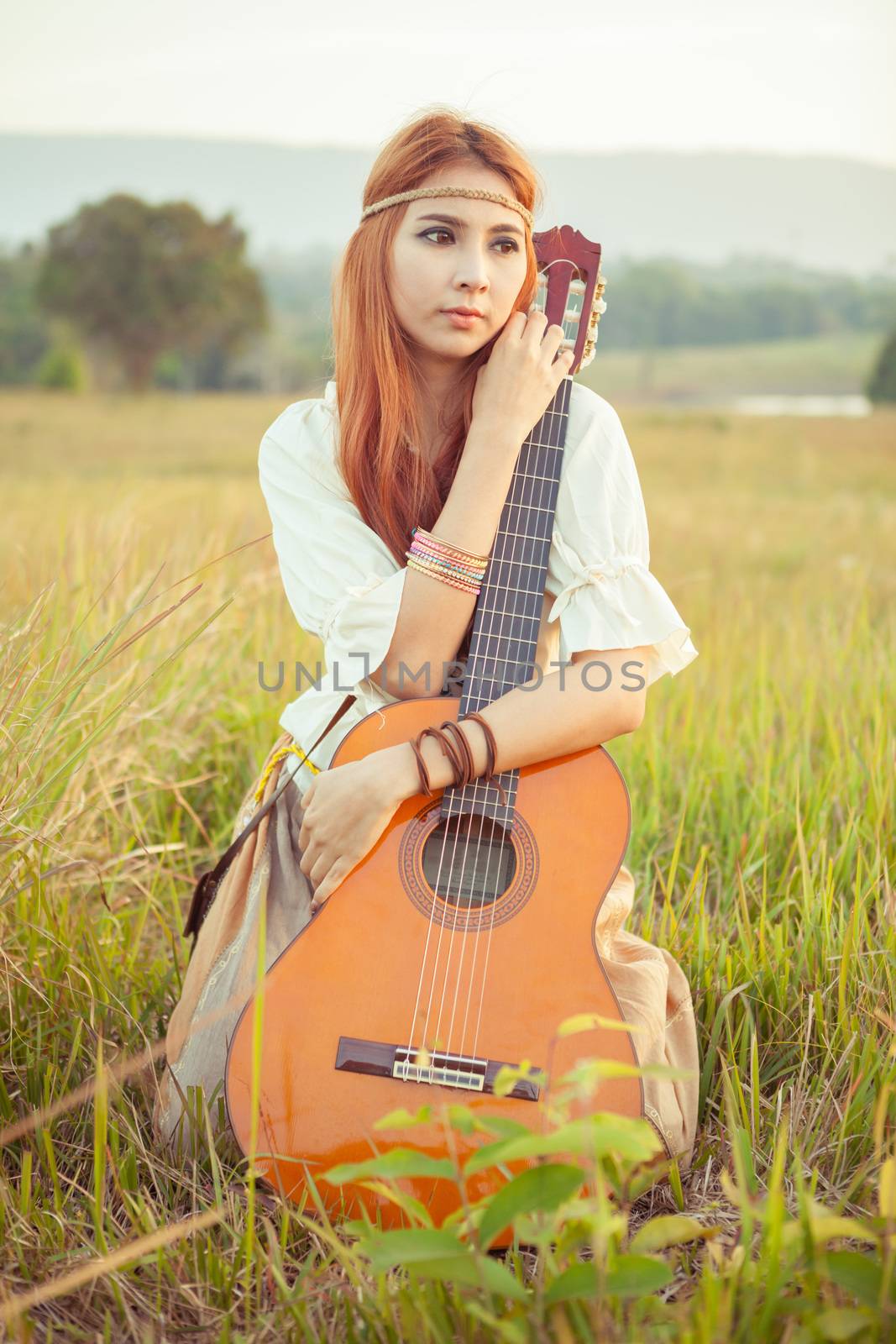 Pretty country hippie girl playing guitar on grass