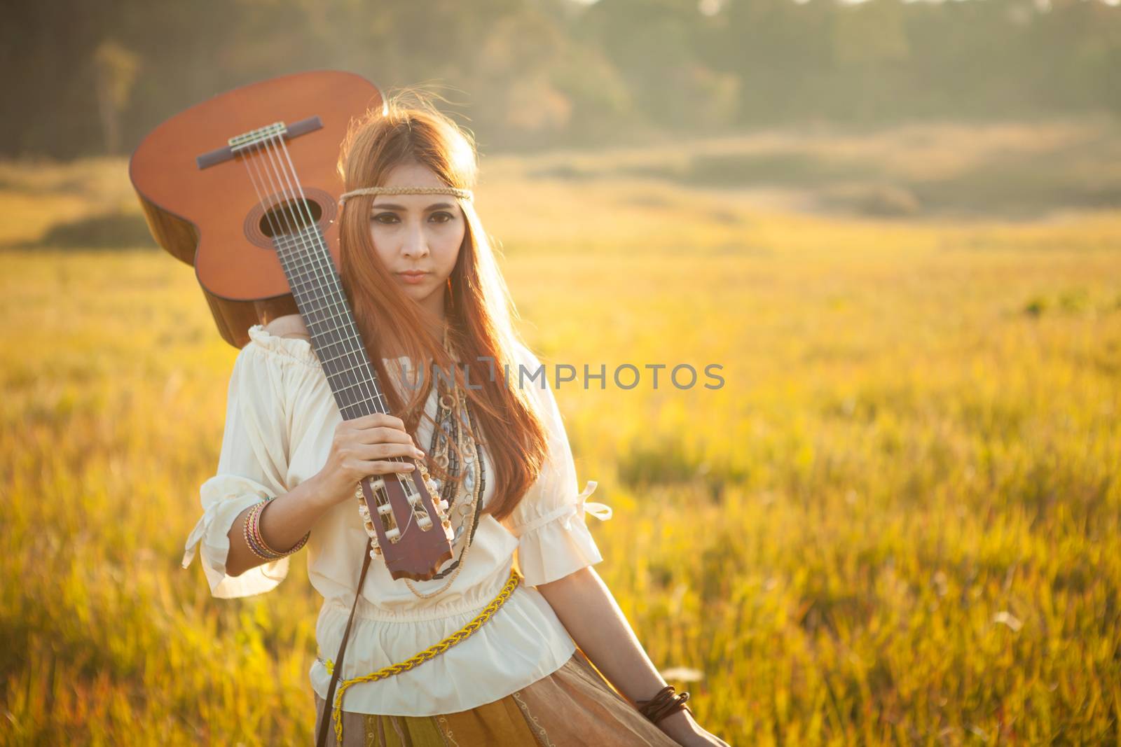 Hippie woman walking in golden field with acoustic guitar