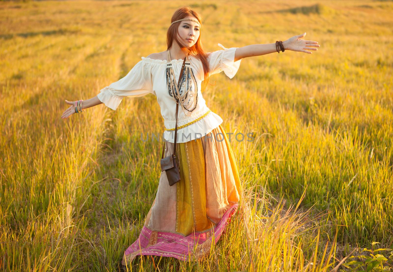 Hippie woman with arms outstretched in golden field on sunset