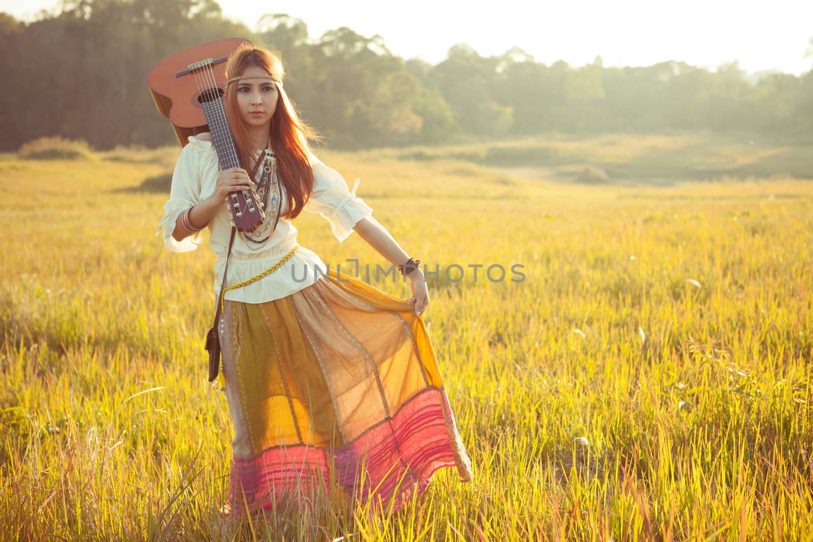 Hippie woman walking in golden field with acoustic guitar