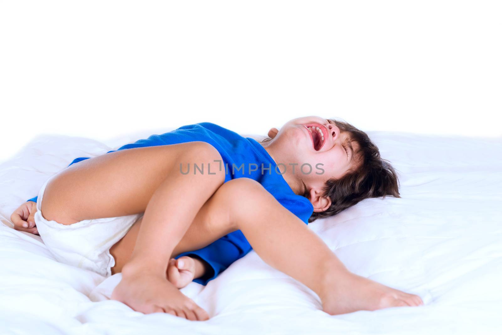 Crying disabled toddler boy lying on white bed