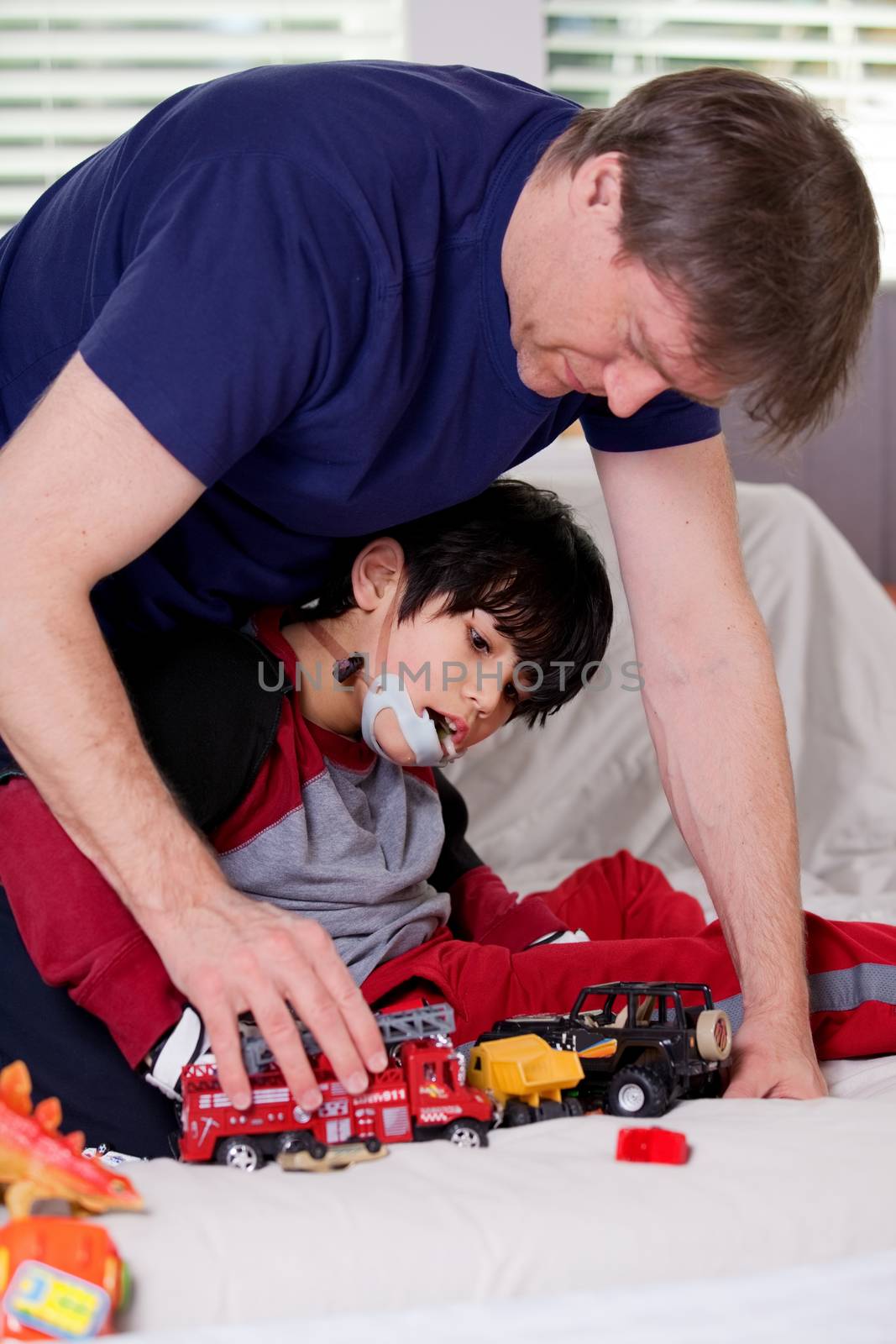 Handsome father playing cars with disabled son on floor mat