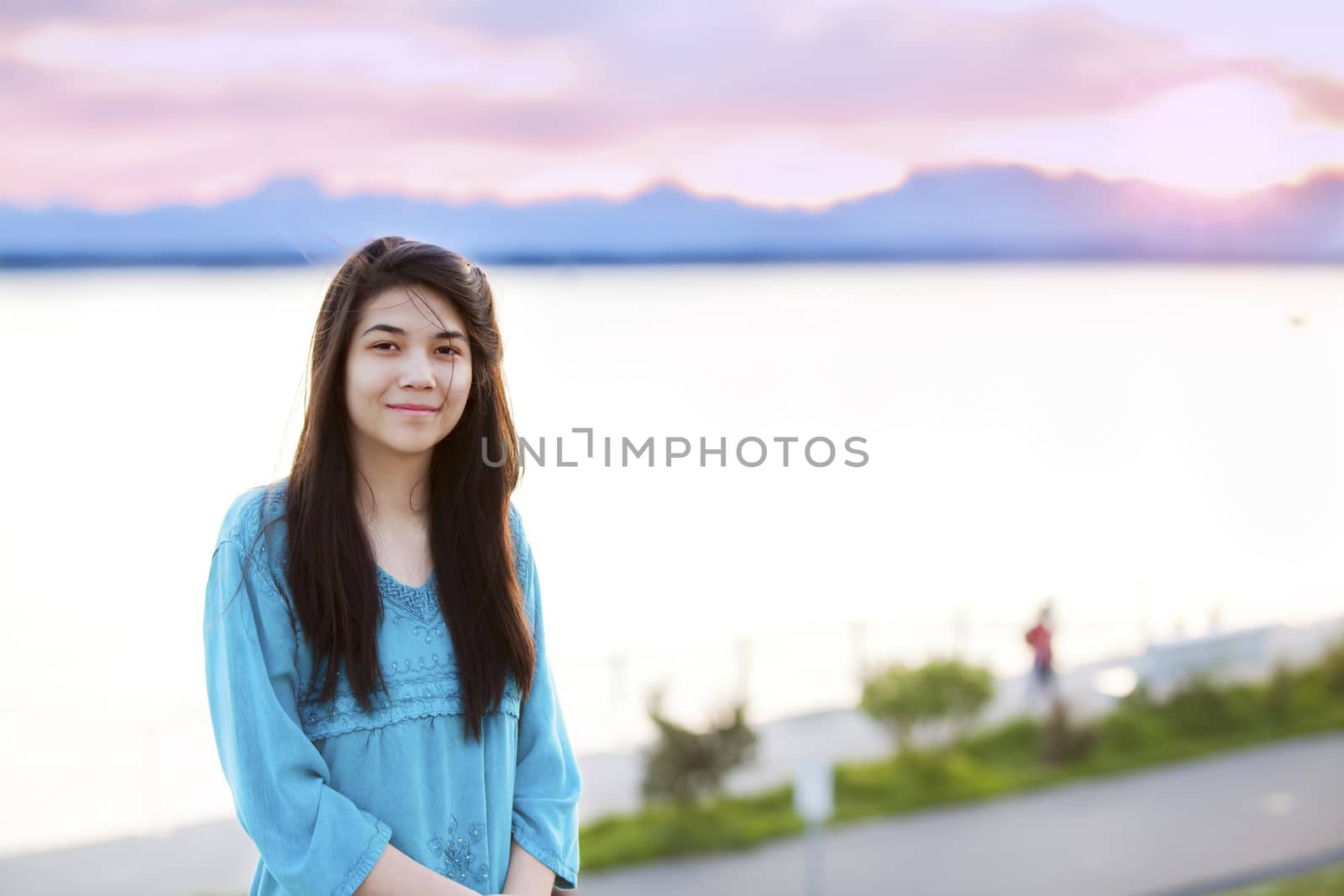 Beautiful biracial young teen girl enjoying outdoors by lake at sunset